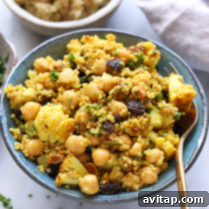 A bowl of couscous with golden roasted cauliflower and chickpeas, garnished with raisins.