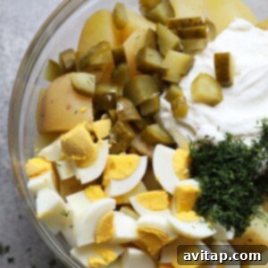 All ingredients for potato salad combined in a bowl, being mixed with a spatula to achieve desired creamy consistency.