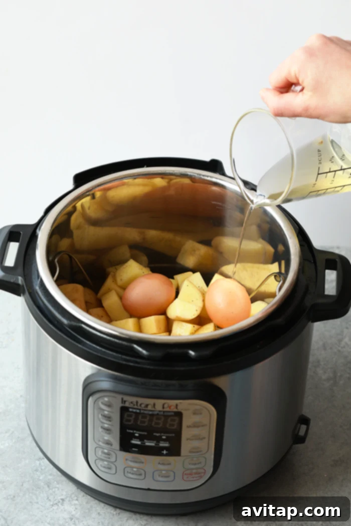 Pouring apple cider vinegar and water into the Instant Pot over chopped potatoes and eggs on a metal rack.