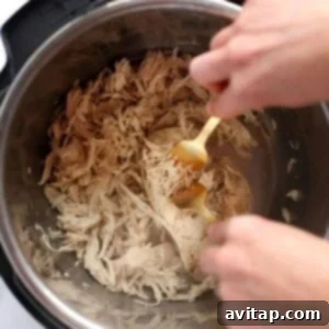 A pair of forks actively shredding cooked Instant Pot chicken breast into tender, fibrous strands.