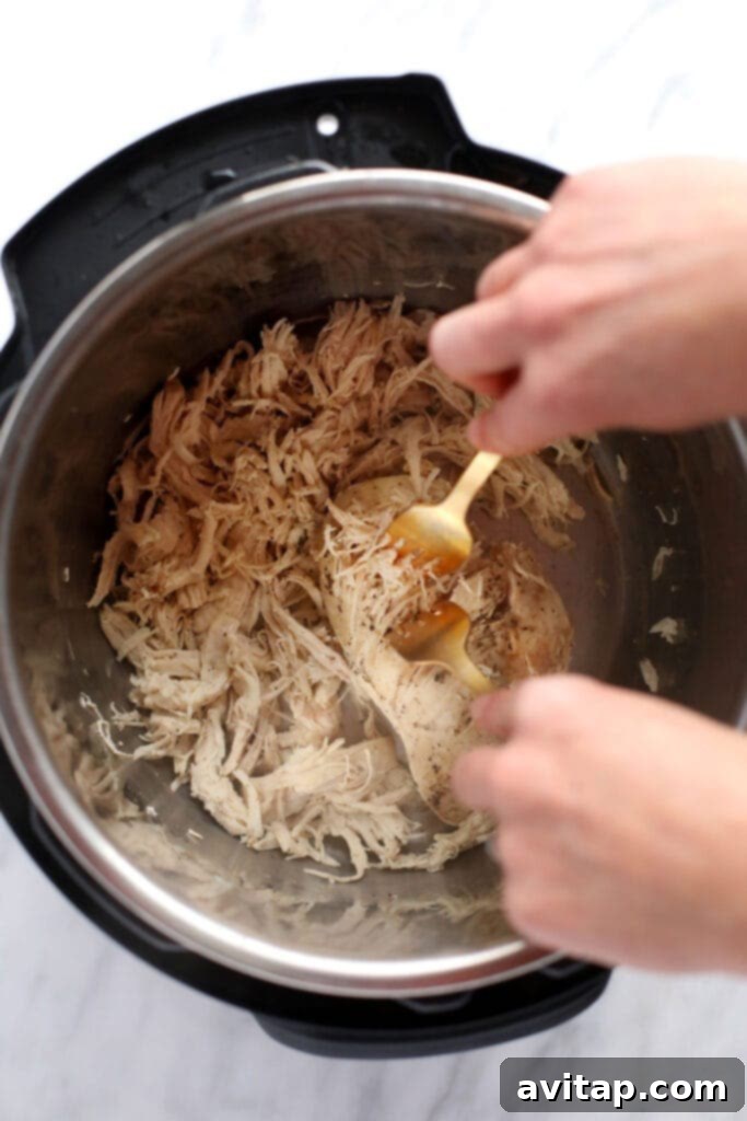Two forks expertly shredding perfectly cooked Instant Pot chicken breast into tender, manageable pieces, demonstrating the ease of preparation.