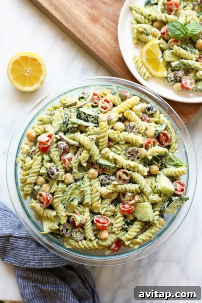 Experience the irresistible flavor of our Creamy Vegan Pesto Pasta Salad, featuring a homemade cashew pesto and fresh, seasonal ingredients. A large bowl of creamy vegan pesto pasta salad garnished with fresh basil leaves, ready to be served.