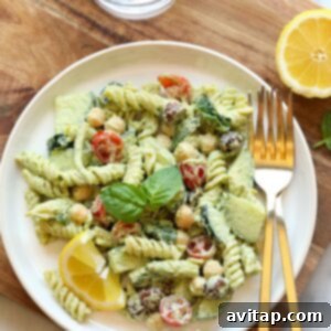 A vibrant Greek pasta salad with chickpeas and lemon wedges, chilled and ready for serving in a glass bowl.