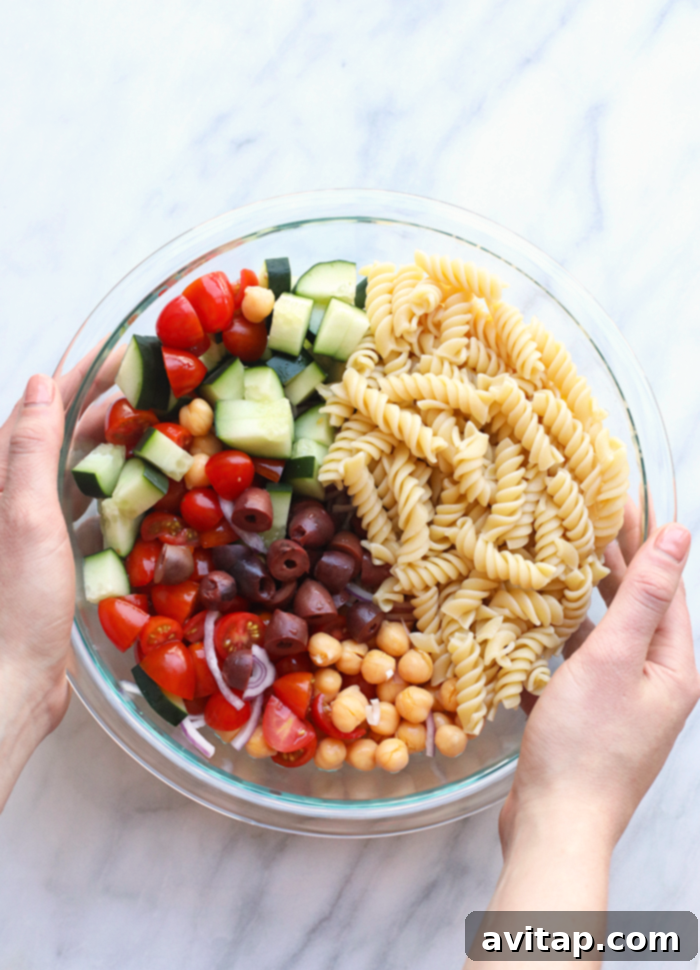 Enjoy this mouthwatering creamy vegan pesto pasta salad as a light lunch or delightful side dish. A large ceramic bowl filled with creamy vegan pesto pasta salad, presented on a rustic wooden table, ready for serving.