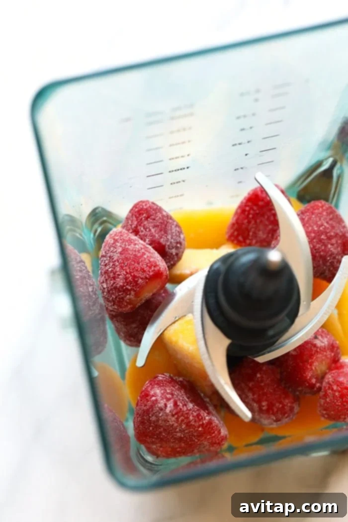 The most delicious summer drink you ever did see! This Strawberry Peach Frose recipe is such a fun frozen drink to make for a crowd. This easy frose recipe calls for a full bottle of rose, frozen strawberries and peaches, rum, and agave nectar! A blender filled with a mix of vibrant frozen fruits, ready to be transformed into frosé.