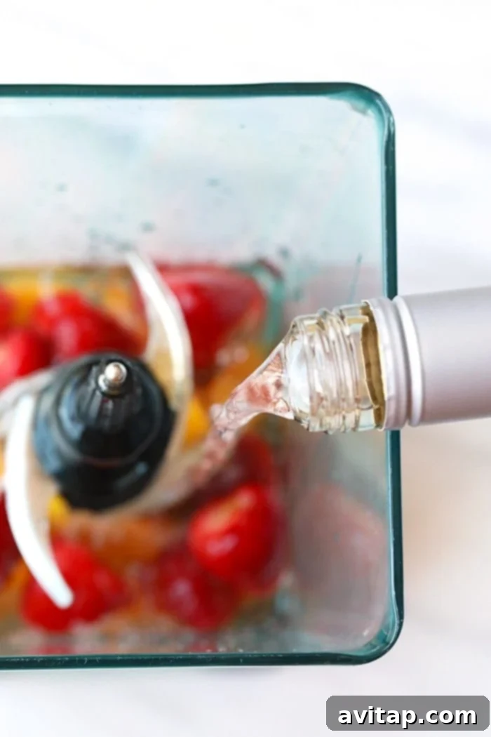This easy frose recipe is made with rose, frozen fruit, rum, and agave nectar. The perfect drink for a summer day! Pouring white rum into a blender filled with rosé and frozen fruit, preparing to blend frosé.