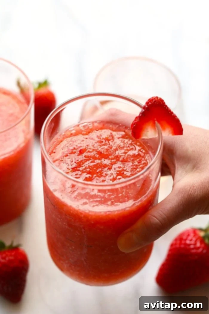 Make this easy frose recipe in less than 10 minutes with whole froen fruit, rose, agave nectar, and rum! A hand holding a beautifully garnished glass of frosé, perfectly chilled for a hot day.