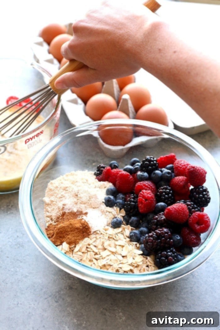 Combining Wet and Dry Ingredients for Berry Oatmeal Cups Mixing triple berry baked oatmeal cup ingredients in a bowl