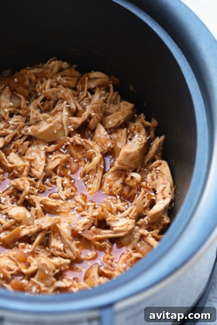 Close-up view of sesame chicken simmering in the slow cooker, coated in a thick, glossy, and aromatic sauce.
