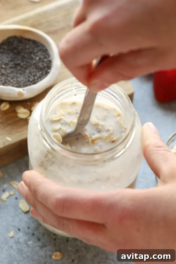Overnight oats being stirred in a glass jar with a spoon.