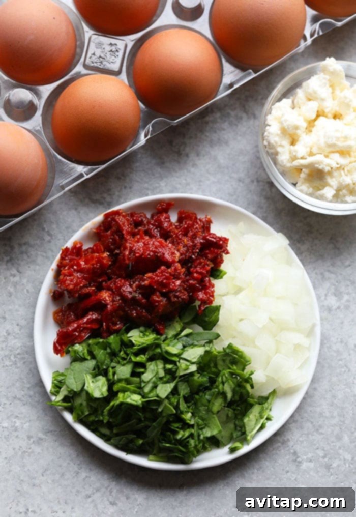 A batch of freshly baked spinach egg muffins with visible chunks of sun-dried tomatoes and feta cheese.
