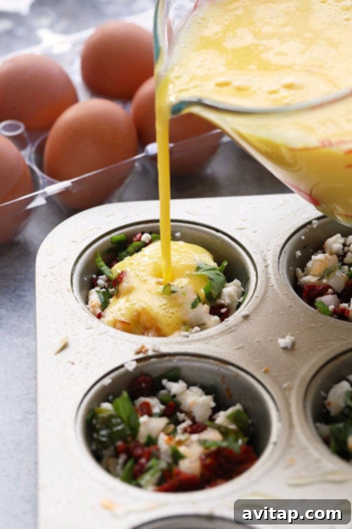 A close-up shot showing eggs being poured into a muffin tin filled with chopped vegetables and feta cheese, ready for baking.