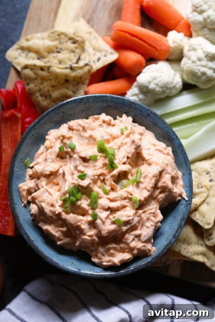 A beautifully presented bowl of buffalo chicken dip, garnished with fresh herbs and served with an assortment of crisp vegetables and crackers, ready to be enjoyed as a protein-packed and flavorful appetizer.