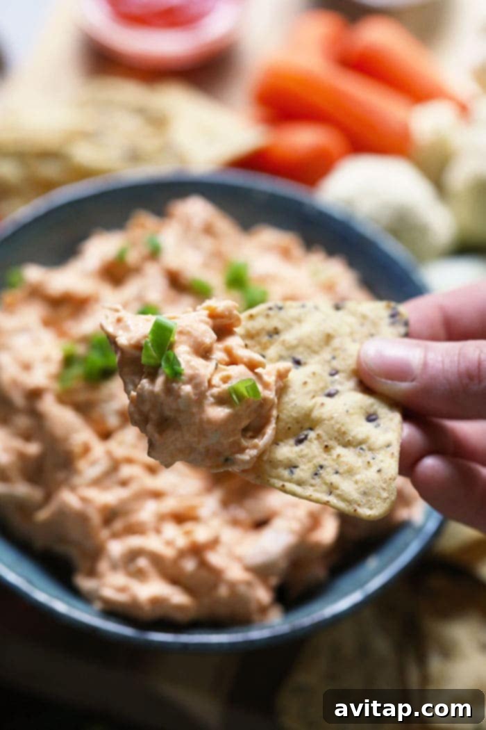 A hand holding a chip generously loaded with creamy buffalo chicken dip, highlighting its texture and inviting appeal for a quick, satisfying bite.
