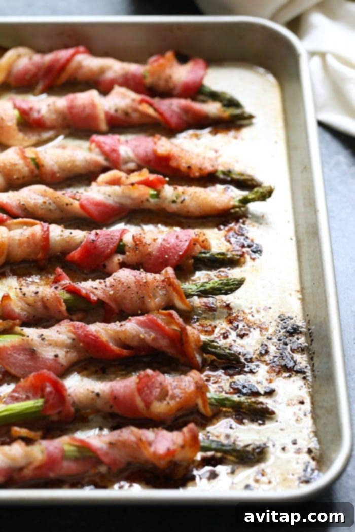 Crispy bacon wrapped asparagus spears on a baking sheet, ready to serve.