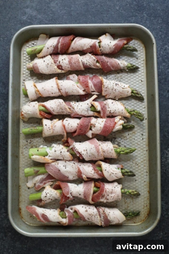 A perfect weeknight side dish, these bacon wrapped asparagus bundles are both easy and delicious. Three bundles of bacon wrapped asparagus on a baking sheet, showing the golden-brown crispy bacon and bright green asparagus.