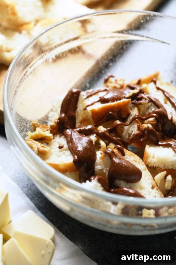 Close-up of cubed sourdough bread, walnuts, and a rich almond butter cinnamon drizzle being mixed in a bowl, illustrating the casserole assembly process.