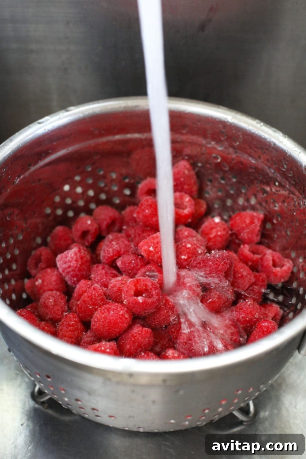 Raspberries being gently washed in a colander before drying.