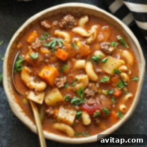 A bowl of hamburger soup with a fork, garnished with fresh herbs, highlighting the hearty and comforting nature of the dish.