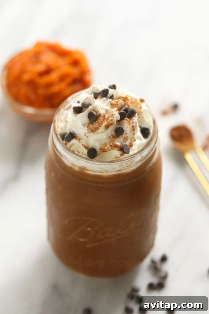 Pumpkin Pie Smoothie in Jar A close-up of a pumpkin coffee smoothie in a mason jar, garnished with whipped topping and a dusting of pumpkin pie spice, ready to be enjoyed.