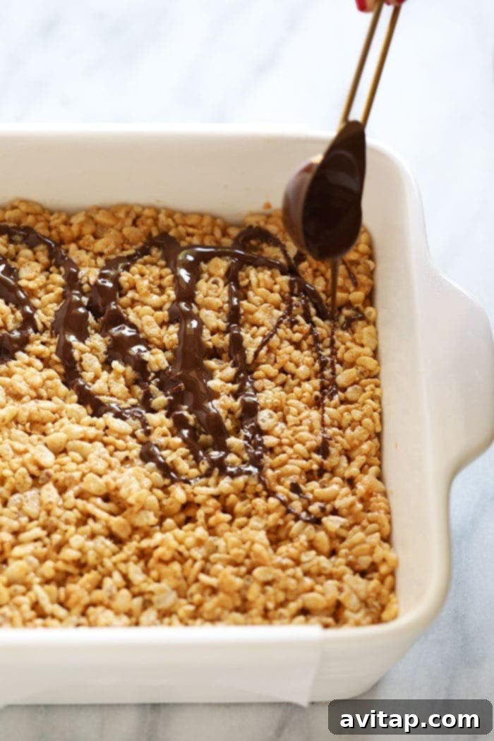 Wholesome Peanut Butter Crunch Bars 4 Rice crispy bars meticulously arranged in a pan, featuring a tempting chocolate drizzle and a generous sprinkle of coarse sea salt, showcasing the final stages of preparation.