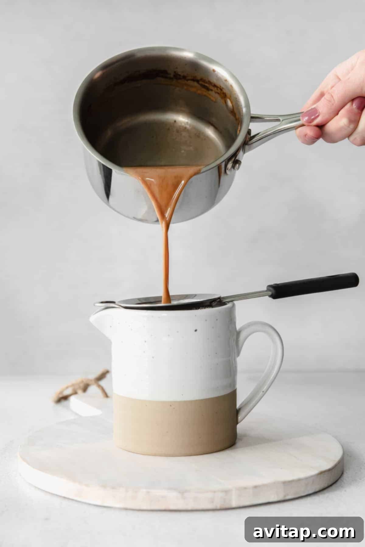 Straining a homemade chai tea latte through a fine sieve into a mug
