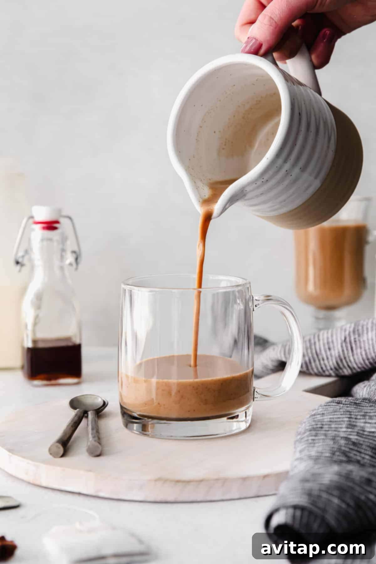 Pouring freshly made chai tea latte into a mug, showing steam rising