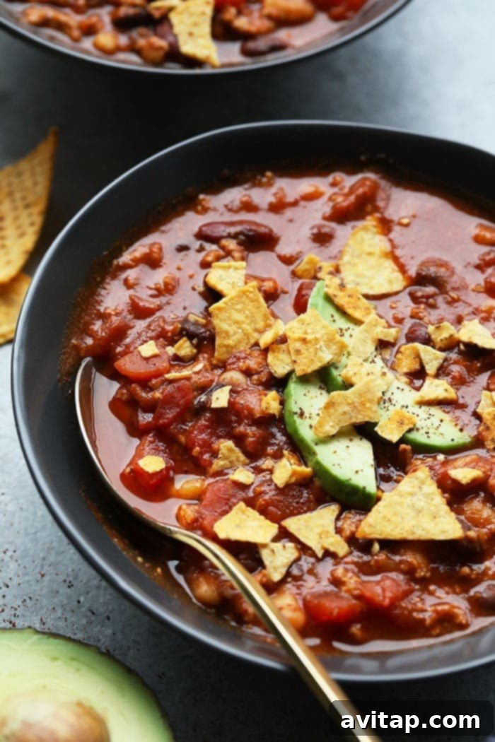 A bowl of healthy turkey chili garnished with fresh avocado slices and crispy tortilla chips.