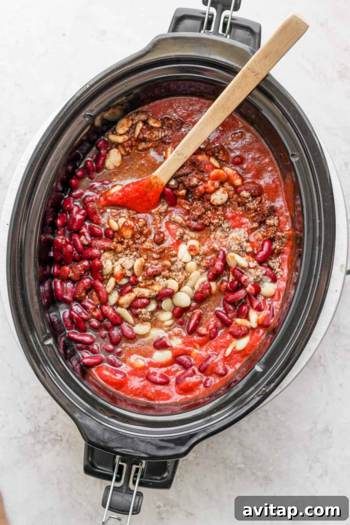 A slow cooker turkey chili simmering gently, with a wooden spoon resting in the rich, thick mixture.