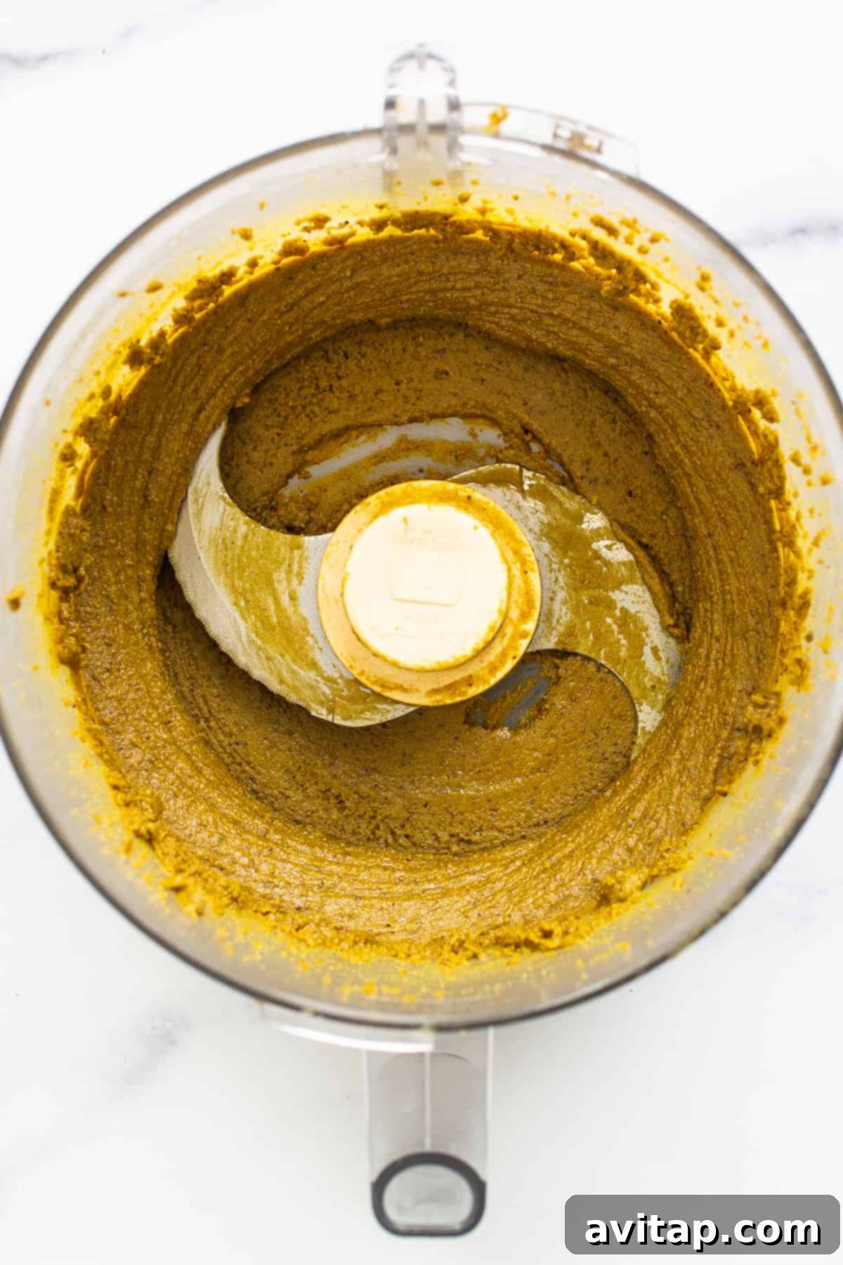 Creamy pistachio butter swirling in a food processor bowl.