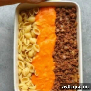 A person holding a hamburger casserole dish with the ingredients before they're mixed together.