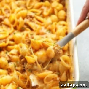 A person scooping hamburger pasta out of a casserole dish.