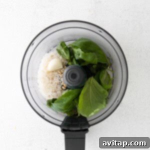 A food processor bowl filled with fresh basil, pine nuts, garlic, and Parmesan cheese, ready for blending into pesto.