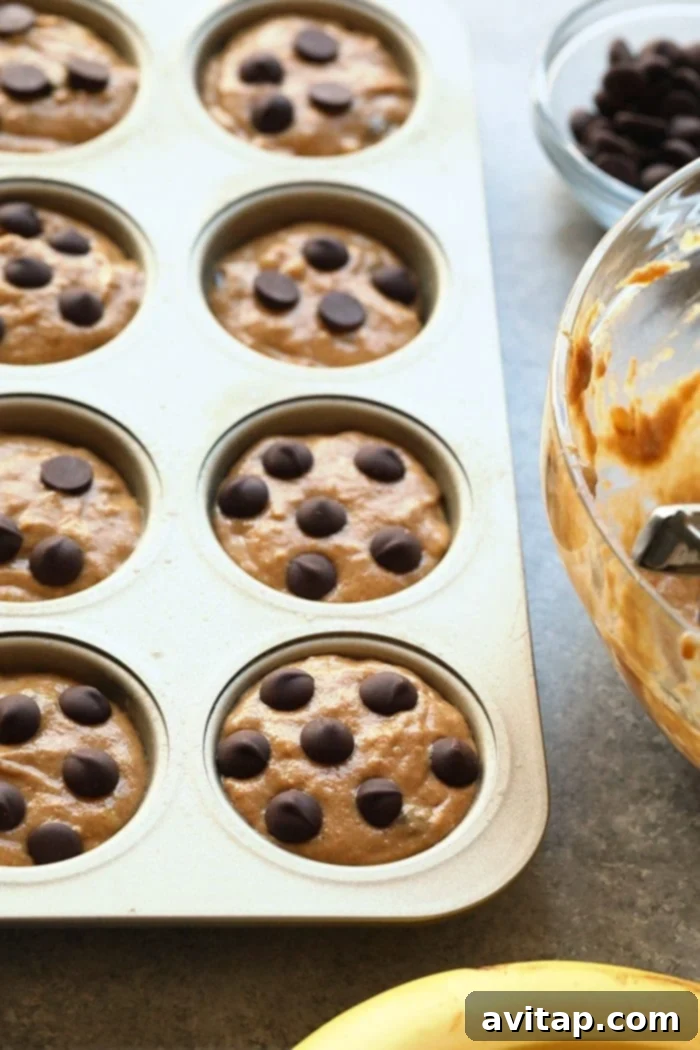 Banana chocolate chip muffin batter meticulously portioned into a lined muffin tin, ready for baking.