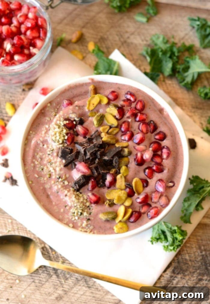 Vibrant pomegranate green smoothie bowl topped with various ingredients.