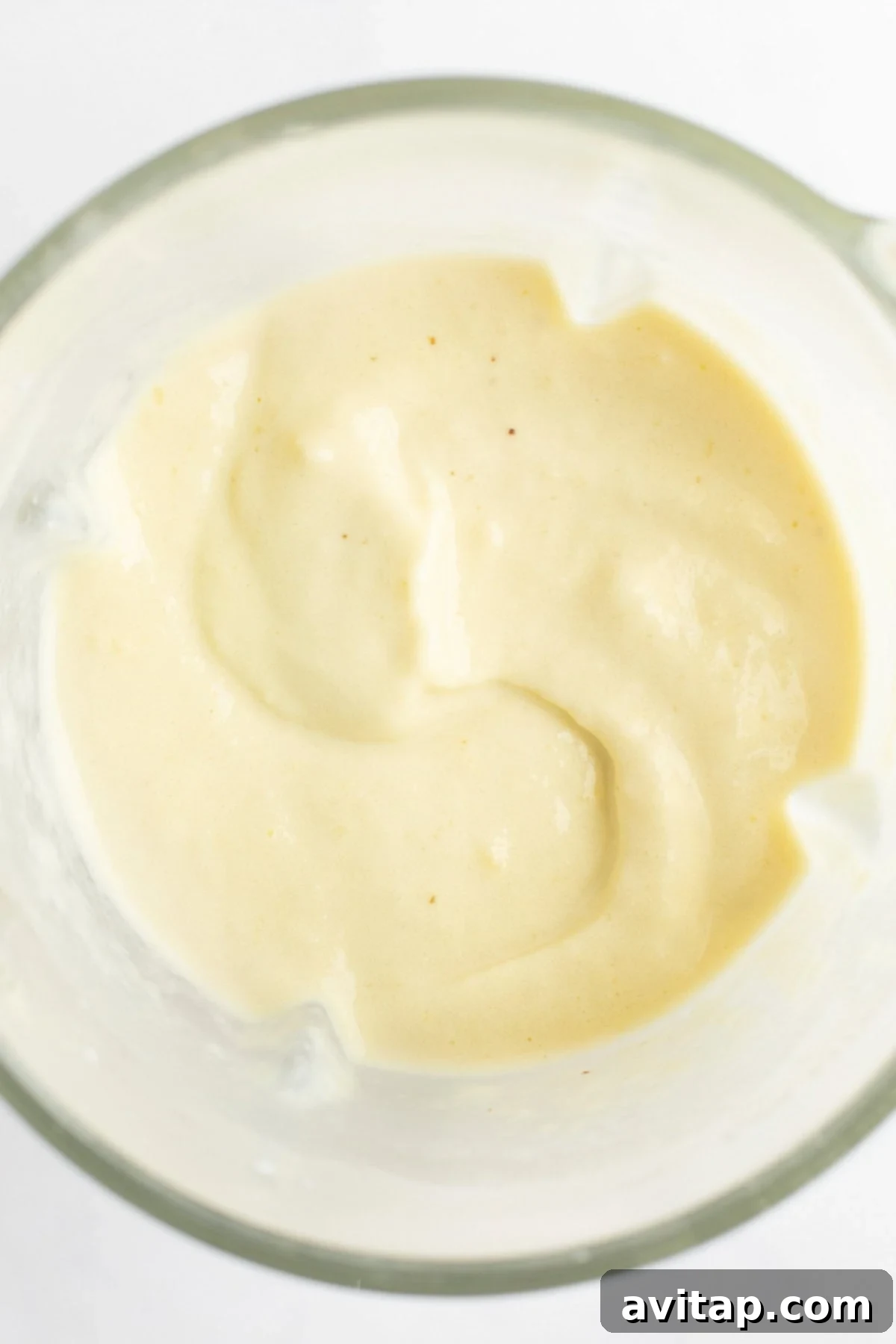 A close-up view of a perfectly smooth, creamy, beige-colored mixture in a bowl, illustrating the ideal texture of a well-blended smoothie.