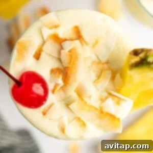 Top view of a creamy tropical cocktail garnished with toasted coconut flakes, a maraschino cherry, and a pineapple slice.