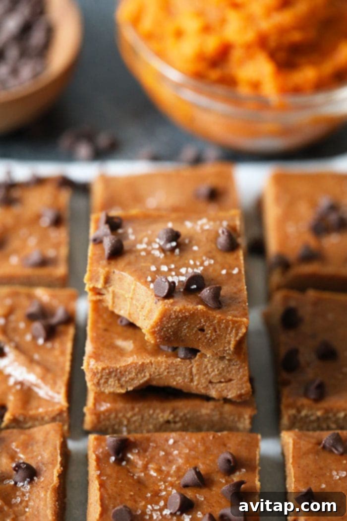A hand reaching for a single square of pumpkin almond butter freezer fudge, highlighting its readiness to eat