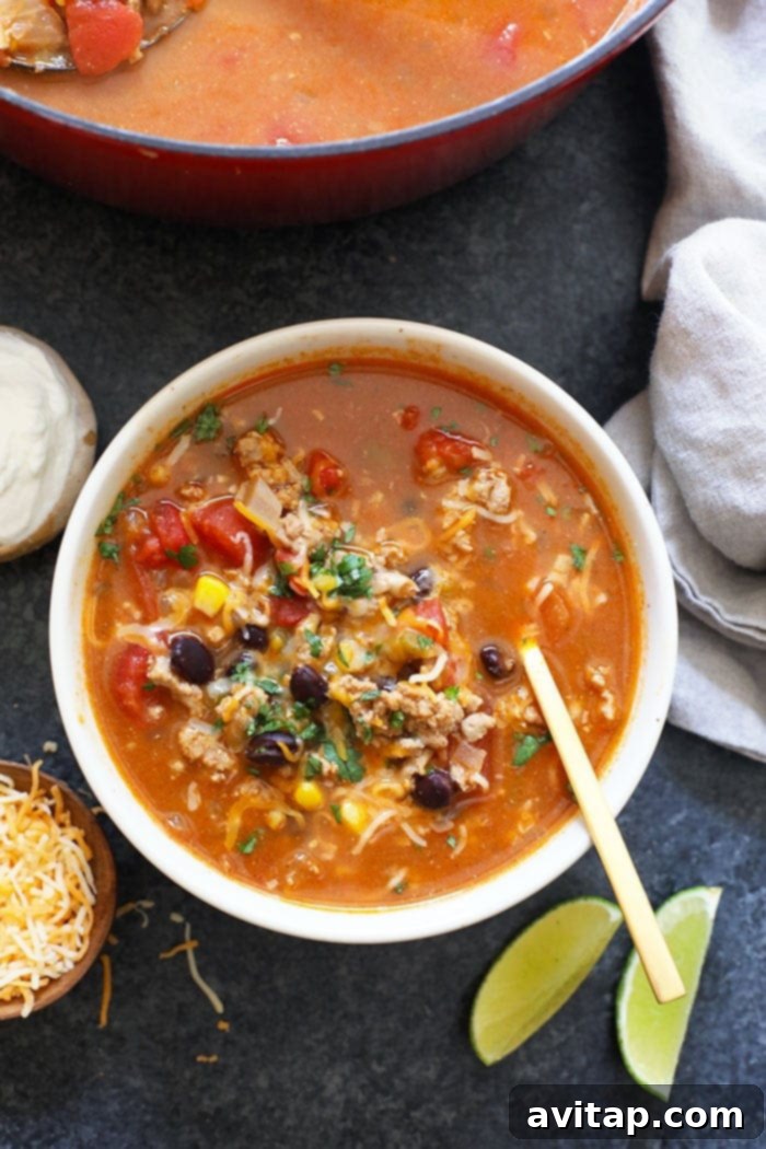 A vibrant bowl of healthy taco soup, richly colored with tomatoes and corn, garnished with fresh cilantro and a dollop of Greek yogurt, ready to be scooped with tortilla chips.