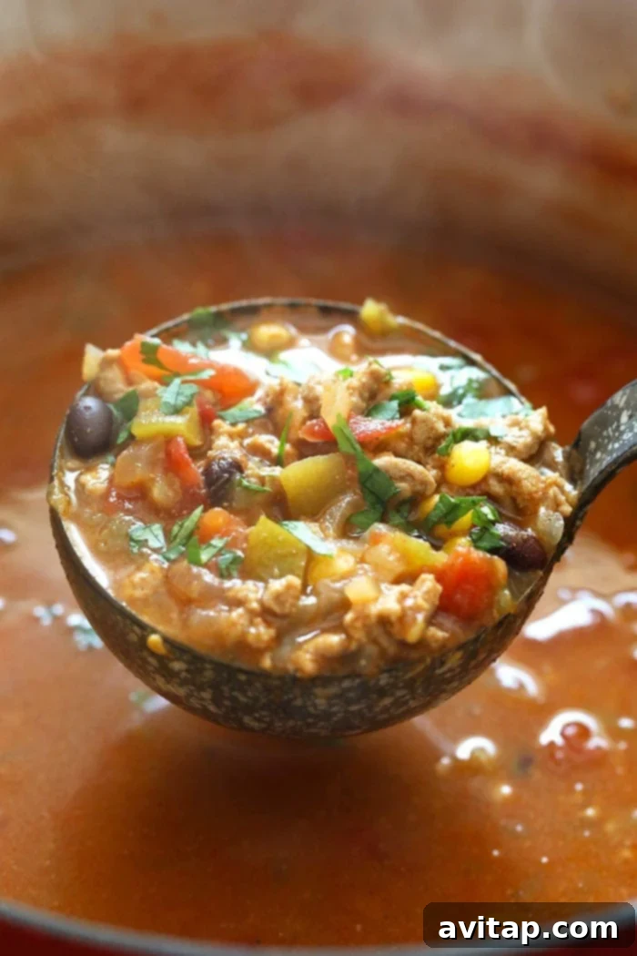 A ladle full of rich, healthy taco soup being served from a large Dutch oven, showcasing its hearty texture, vibrant ingredients like corn and beans, and steam rising from the warm broth.