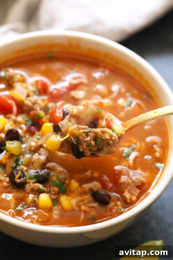 A close-up shot of a spoonful of chunky, rich taco soup being lifted from a bowl, showcasing the generous amounts of beans, corn, and ground meat, inviting viewers to experience its hearty texture.