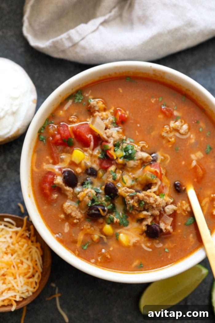 A beautifully presented bowl of taco soup, richly garnished with fresh toppings such as Greek yogurt, cilantro, and shredded cheese, set against a rustic wooden background, enticing viewers with its appeal and readiness for enjoyment.