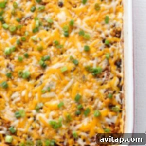 A chicken casserole topped with melted cheese and garnished with fresh green onions after baking.