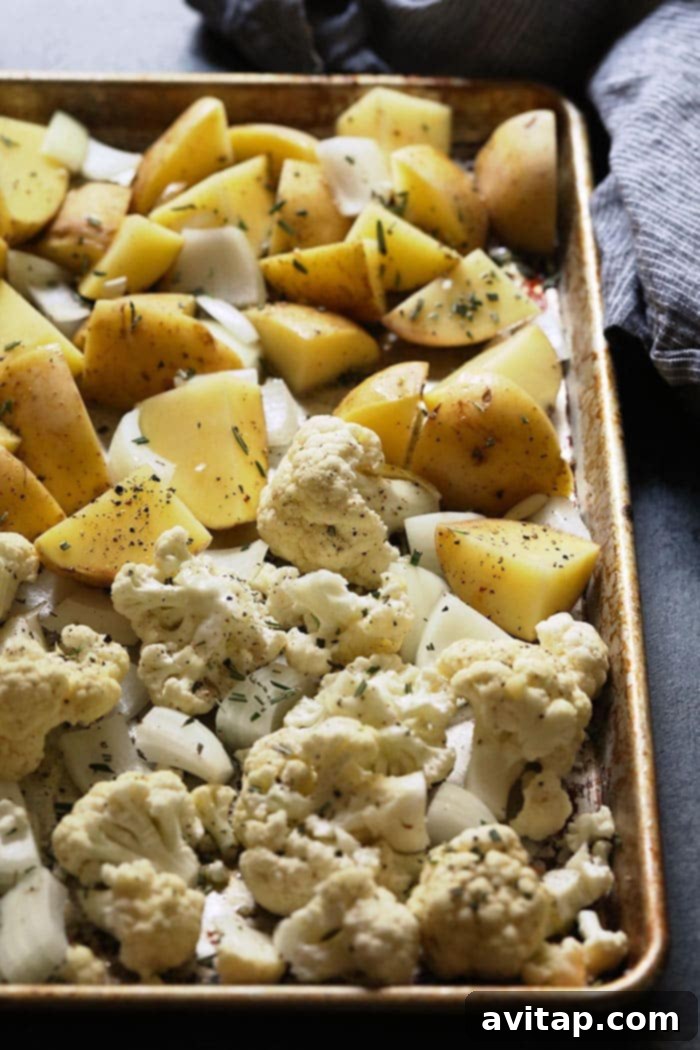 Seasoned diced potatoes and cauliflower florets with garlic and onion on a baking sheet, ready for roasting