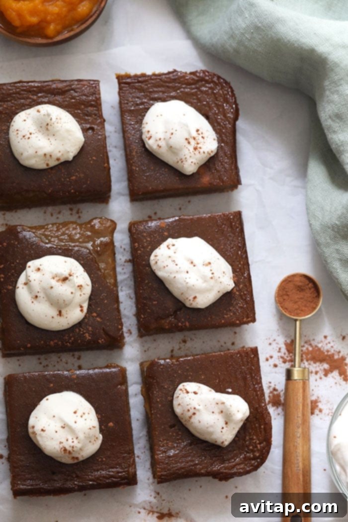 A festive platter showcasing multiple healthy pumpkin pie bars, each exquisitely topped with a swirl of white whipped cream, arranged beautifully for a holiday or fall gathering.