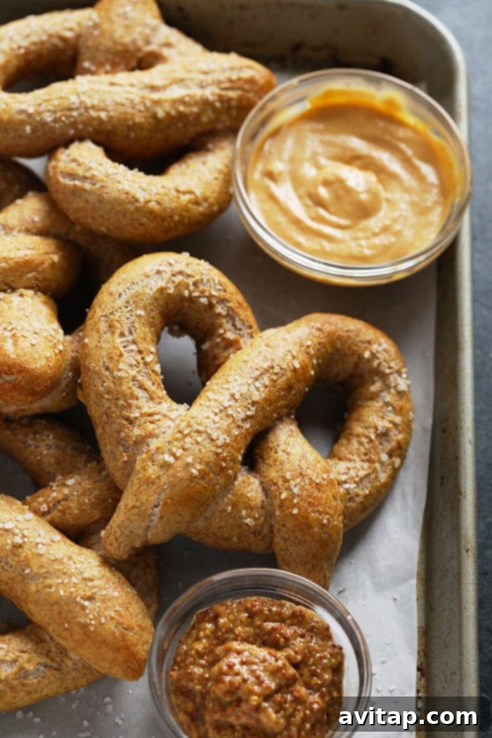 Wholesome Homemade Soft Pretzels 9 Two soft pretzels, one with coarse salt and another with cinnamon sugar, on a baking sheet.