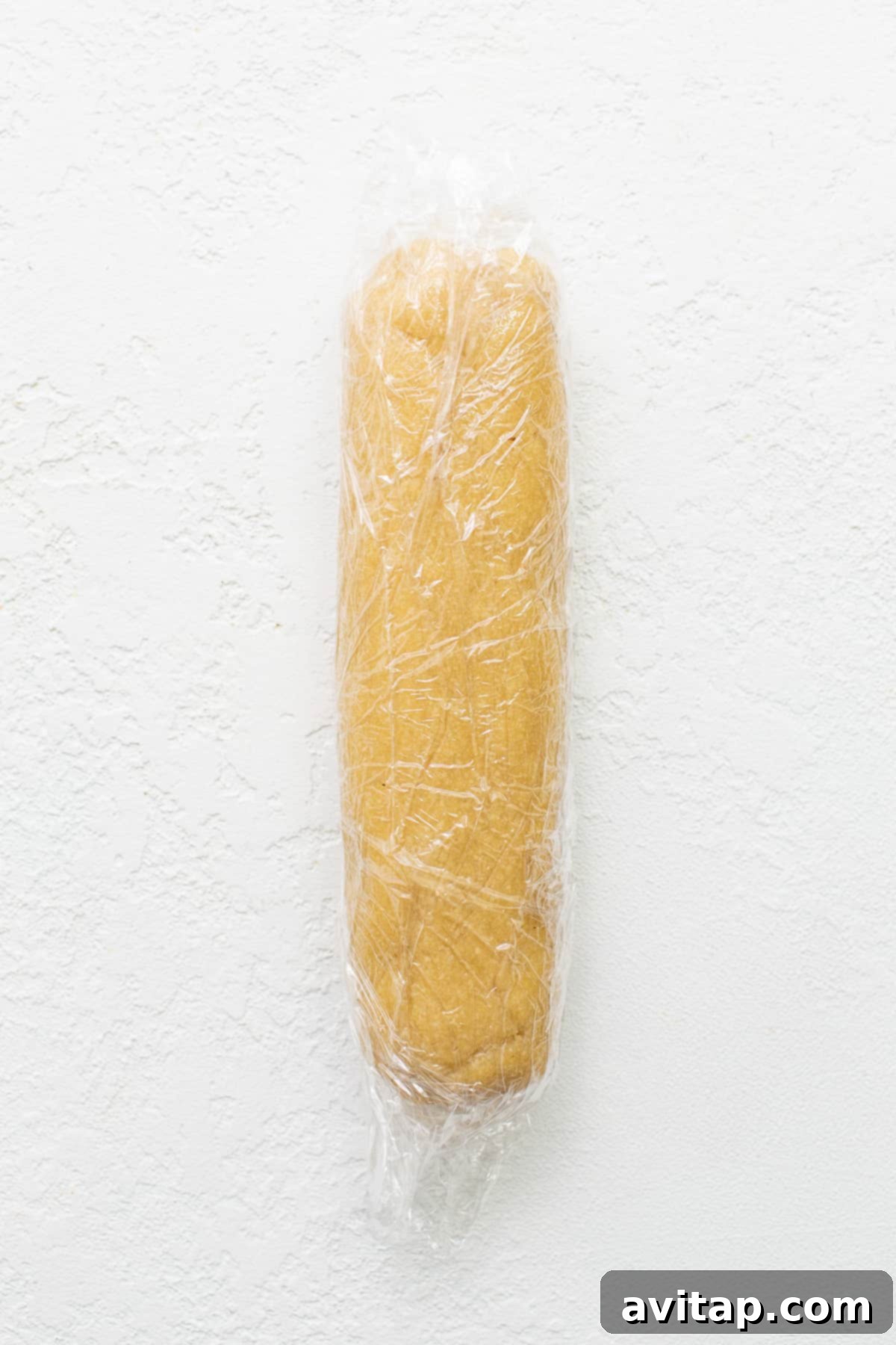 Freshly prepared almond flour cookie dough, meticulously shaped into a log and wrapped in plastic for chilling.
