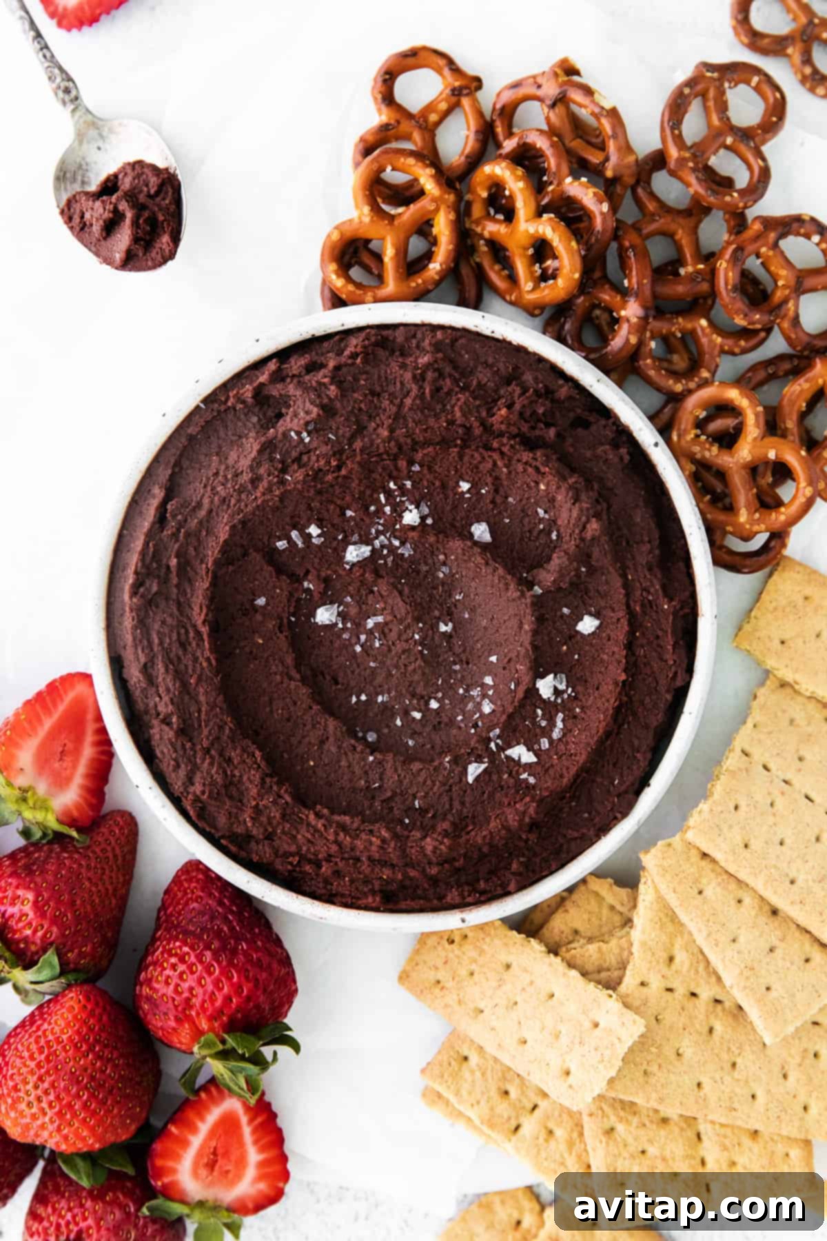 Creamy chocolate hummus served in a bowl with a colorful assortment of pretzels, graham crackers, and fresh strawberries for dipping.