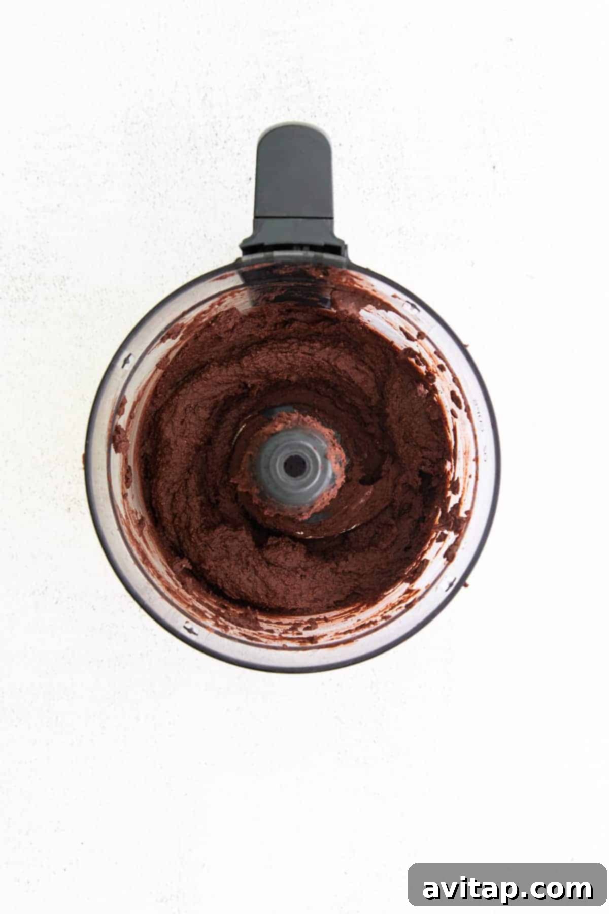 The chocolate hummus ingredients being blended smoothly inside a high-speed food processor, illustrating the consistency development.