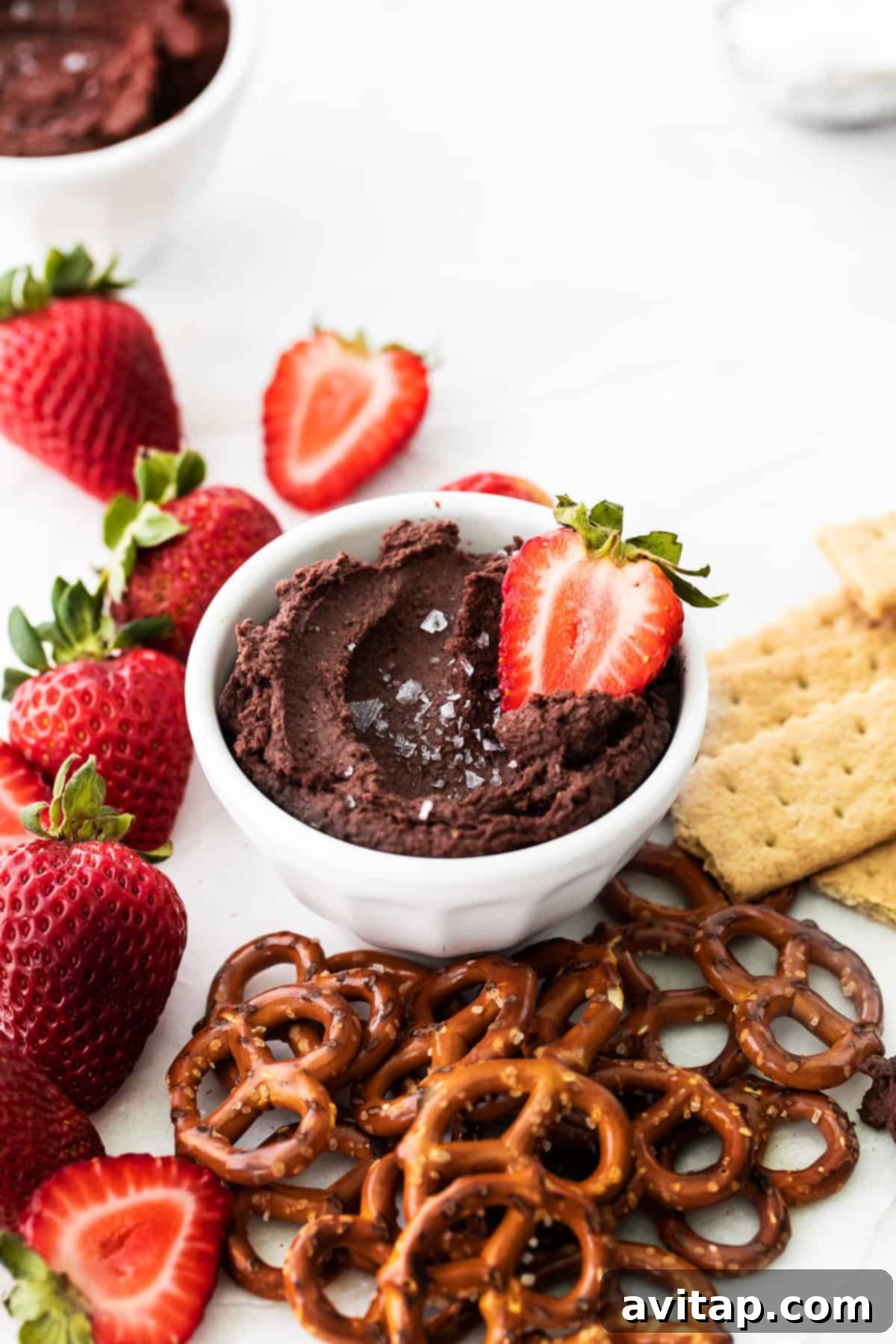 A fresh strawberry being dipped into a bowl of creamy chocolate hummus, showcasing the perfect consistency and delicious pairing.